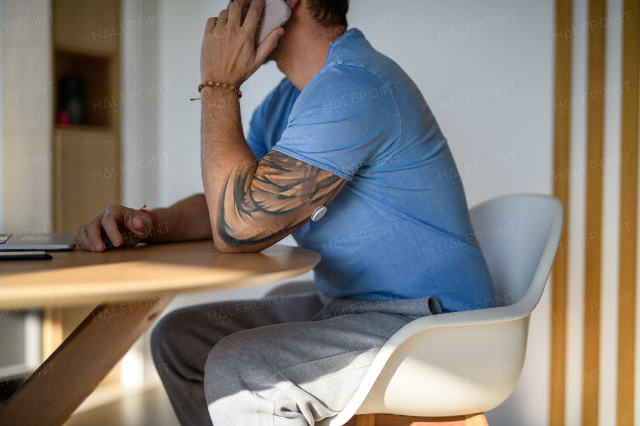 Diabetic man with CGM sensor sitting at table and making phone call.