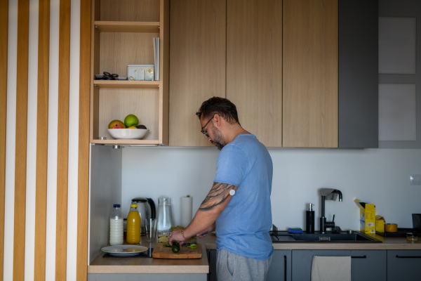 Diabetic man with CGM sensor standing in kitchen and making healthy breakfast.