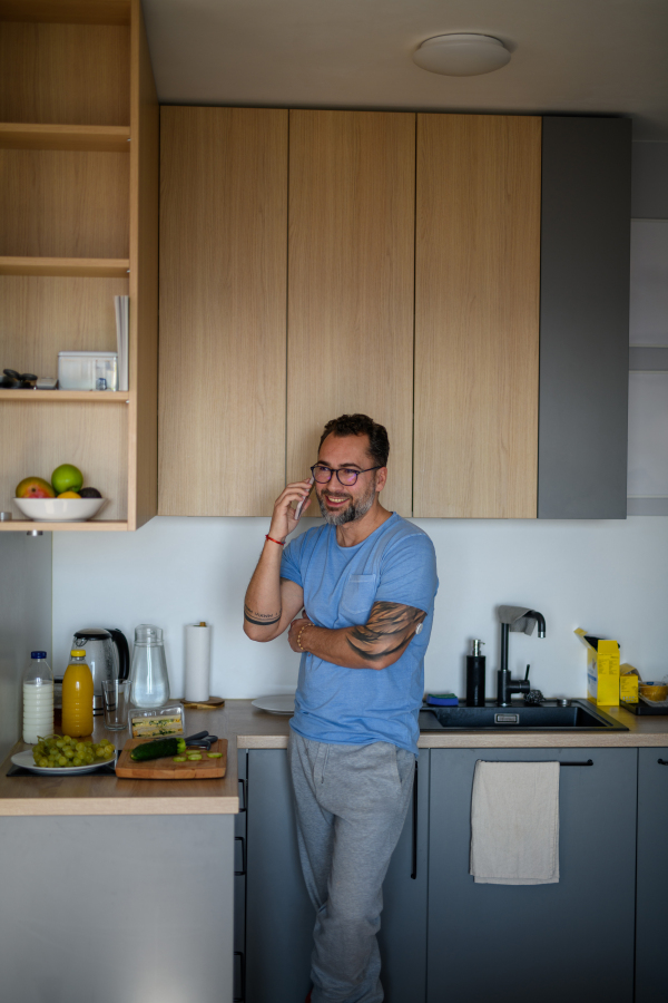 Diabetic man with CGM sensor standing in kitchen and making phone call.