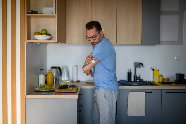 Diabetic man with CGM sensor standing in kitchen and making healthy breakfast.