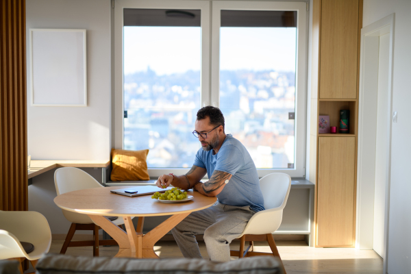 Diabetic man with CGM sensor eating grapes in the morning, sitting at table alone.