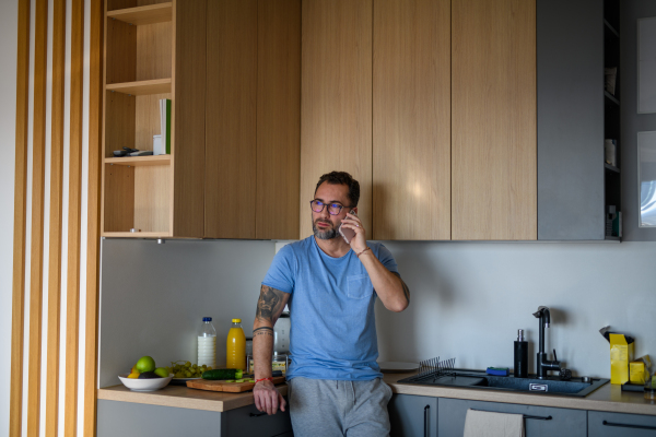 Diabetic man with CGM sensor standing in kitchen and making phone call.