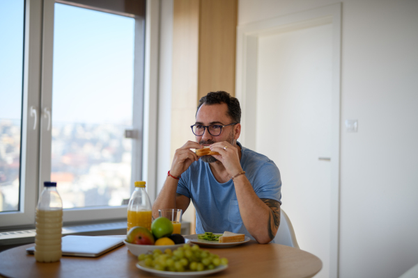 Diabetic man with CGM sensor having healthy breakfast, eating alone at table.