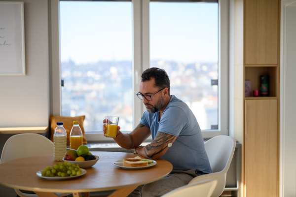 Diabetic man with CGM sensor having healthy breakfast, eating alone at table.