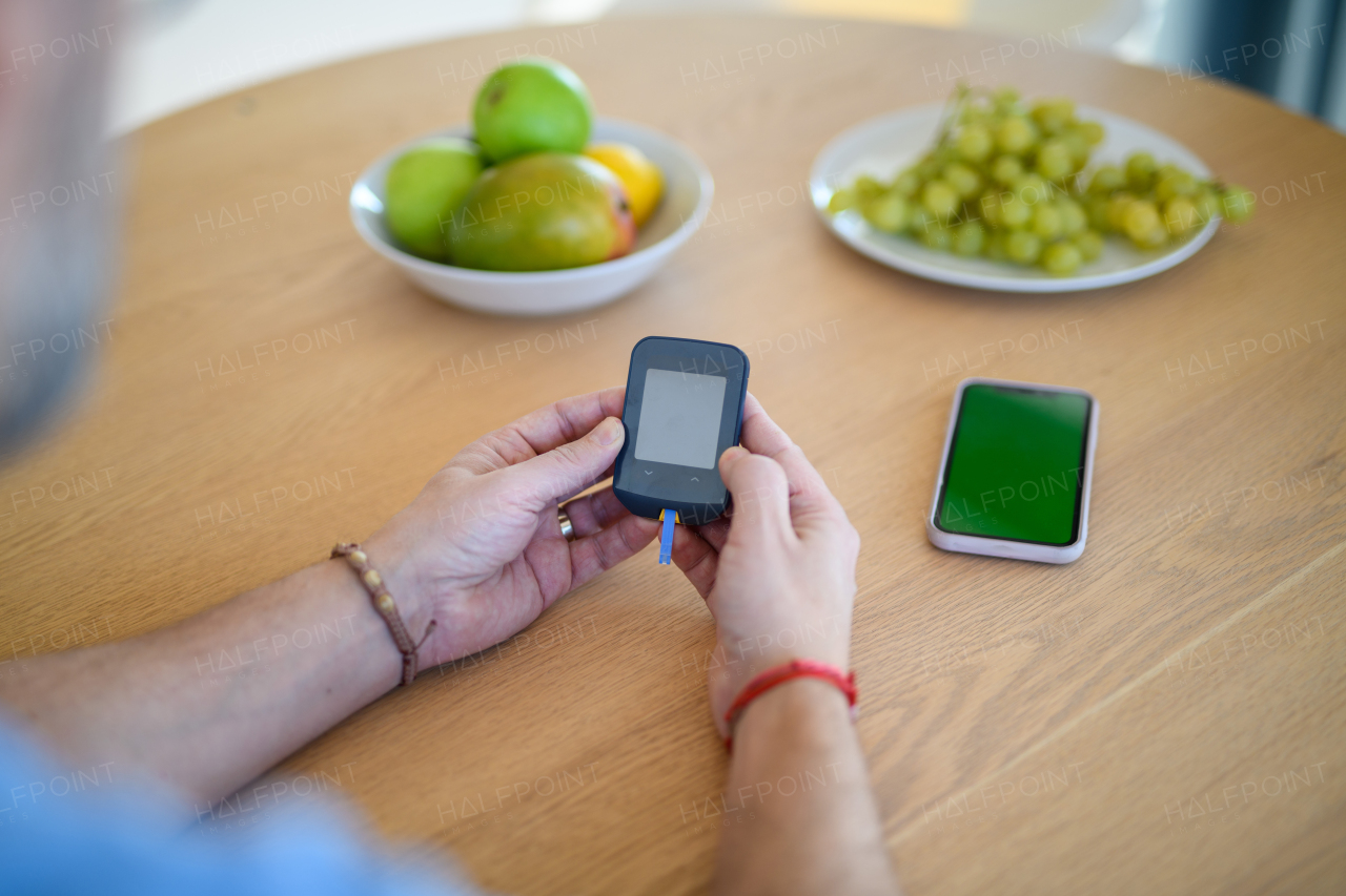 Close up of diabetic man holding blood glucose meter to check blood sugar.