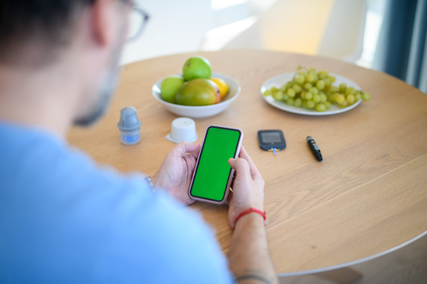 Diabetic man is checking his blood glucose level using smartphone app. Smartphone with green screen.