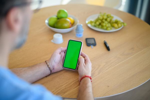 Diabetic man is checking his blood glucose level using smartphone app. Smartphone with green screen.