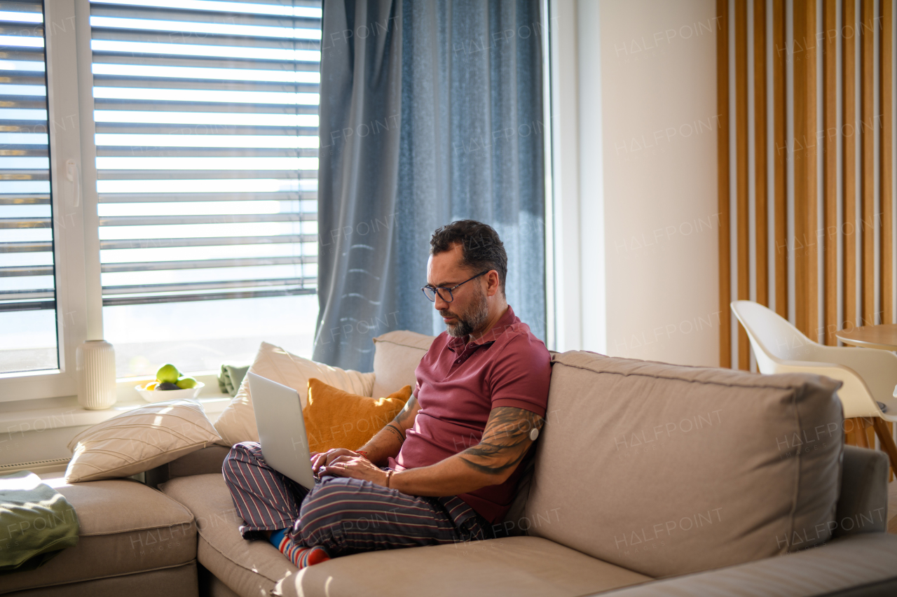 Diabetic man with CGM sensor on arm sitting on sofa and working on laptop.