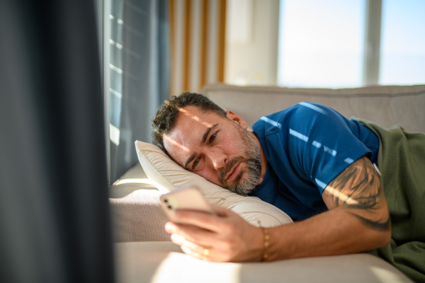 Tired diabetic man lying in bed checking his blood sugar in a mobile app.