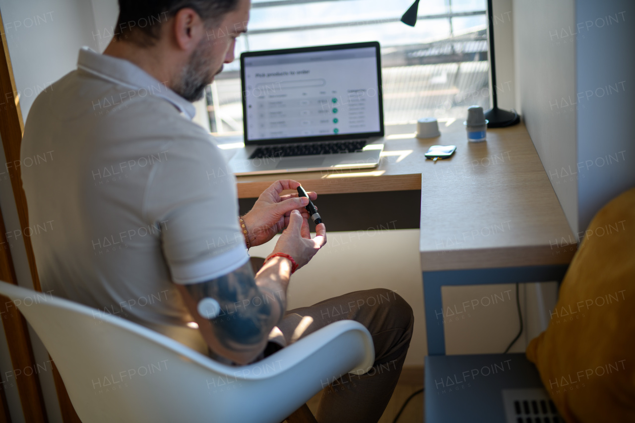 Diabetic man checking his blood sugar at home, using lancet to prick his finger for blood sample.