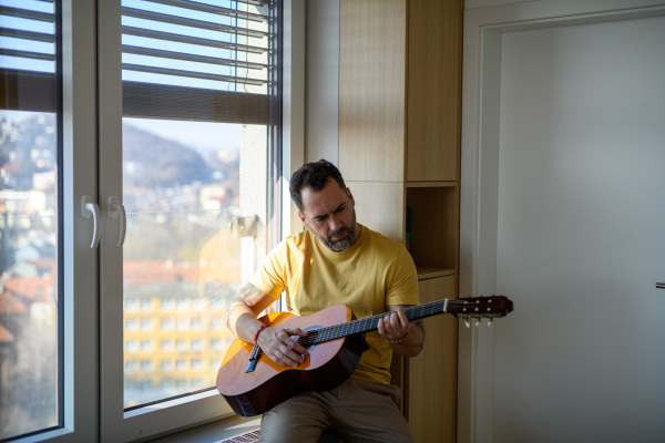 Diabetic man with CGM sensor on arm playing on guitar, spending day at home.