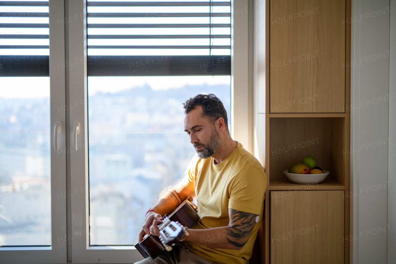 Diabetic man with CGM sensor on arm playing on guitar, spending day at home.