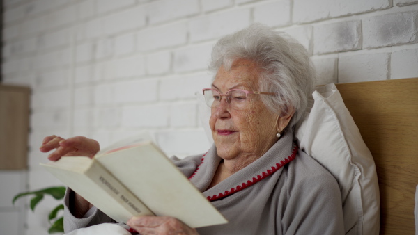 A senior lady smiling while reading a book, lying in the bed.