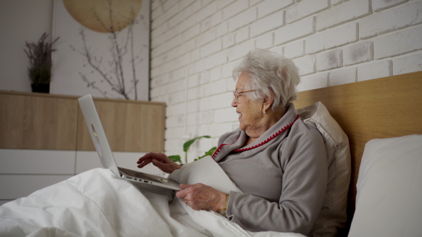 Senior woman lying in bed, working on laptop.