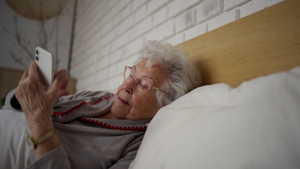 A senior woman lying in bed and using smartphone, looking at screen.