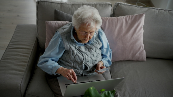 A senior woman using laptop on her own, shopping online with credit card.