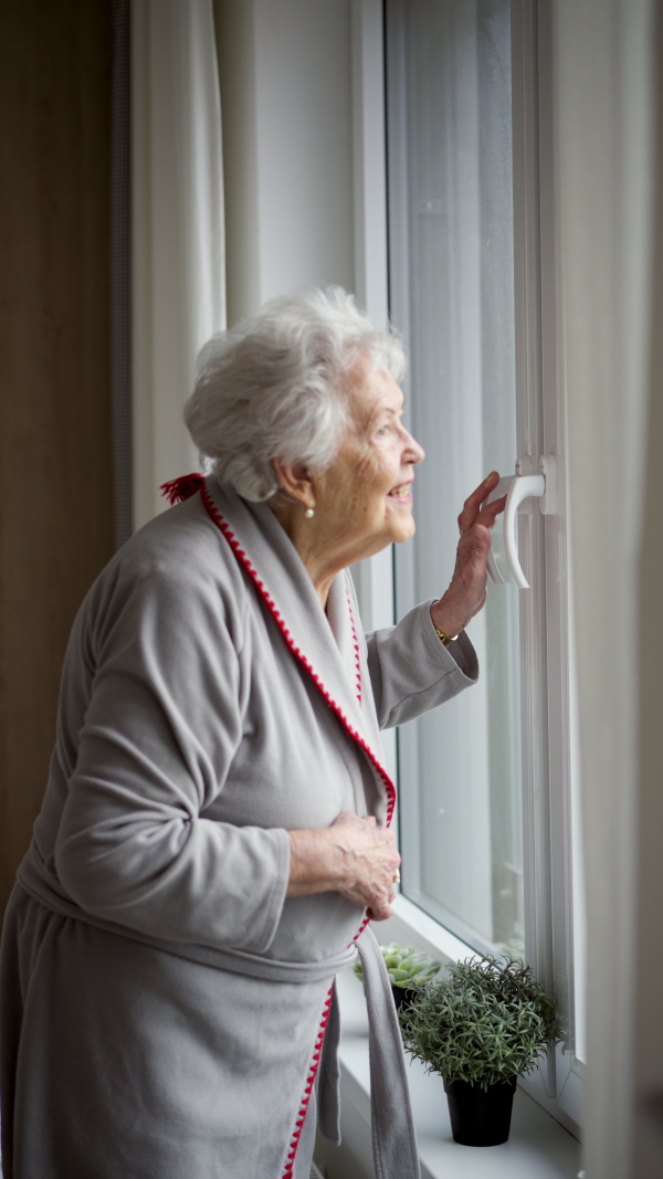 Beautiful senior woman looking out of window, expecting a visitor.