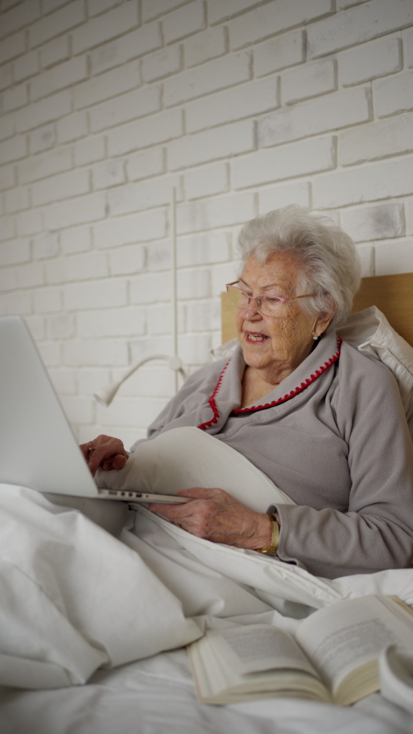 Senior woman lying in bed, working on laptop.