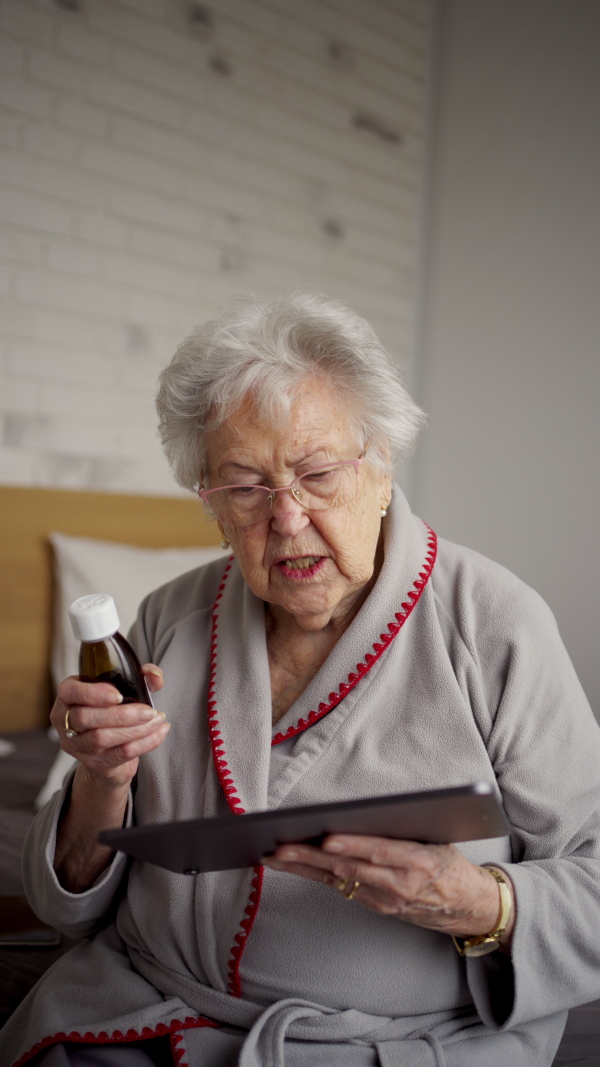 Senior woman reading a medication leaflet and dosage instructions on tablet. Managing medication for seniors.