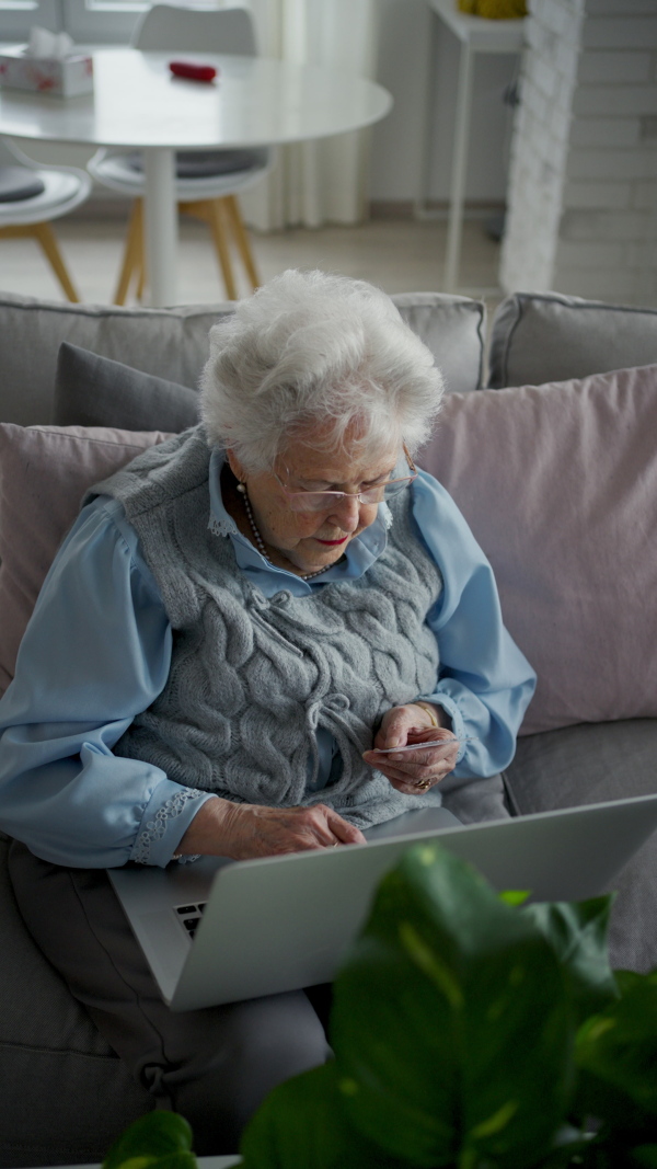 A senior woman using laptop on her own, shopping online with credit card.