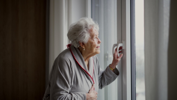 Beautiful senior woman looking out of window, expecting a visitor.