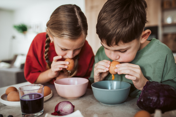 Siblings preparing egshells for easter egg decorating. Blowing out eggs. Kids craft project.