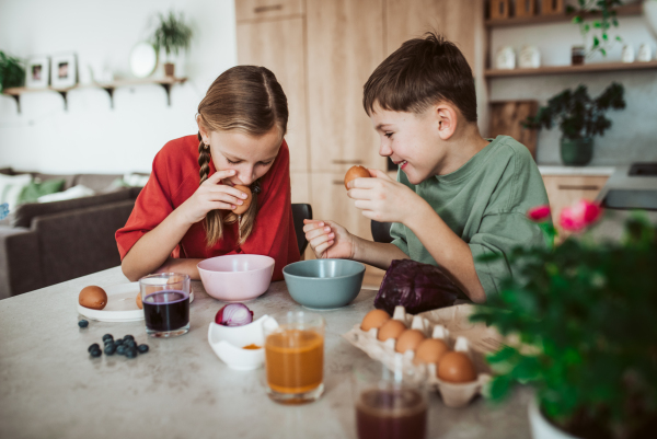 Siblings preparing egshells for easter egg decorating. Blowing out eggs. Kids craft project.