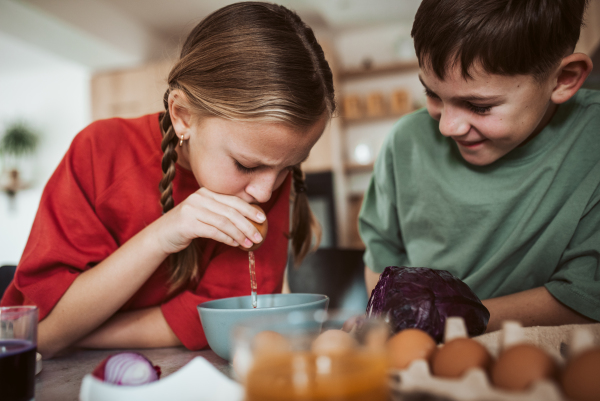 Siblings preparing egshells for easter egg decorating. Blowing out eggs. Kids craft project.