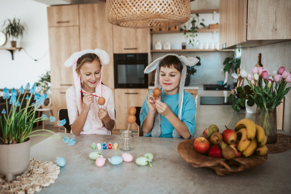 Girl and boy paiting eggs for easter. Siblings decorate egshells for easter egg decorating.