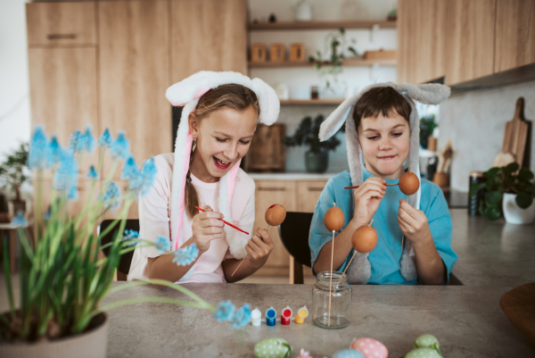 Girl and boy paiting eggs for easter. Siblings decorate egshells for easter egg decorating.