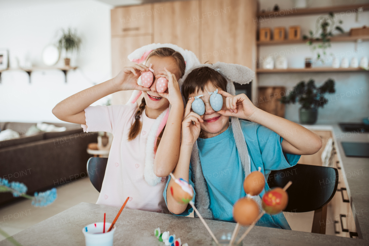 Girl and boy holding decorated easter eggs in front of eyes. Siblings decorate egshells for easter egg decorating.