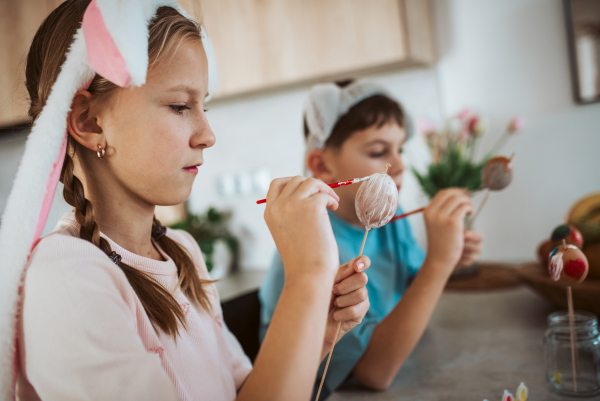 Girl and boy paiting eggs for easter, wearing bunny ears. Siblings decorate egshells for easter egg decorating.