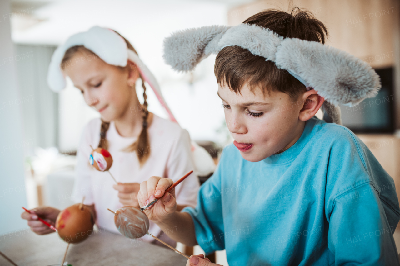 Girl and boy paiting eggs for easter, wearing bunny ears. Siblings decorate egshells for easter egg decorating.