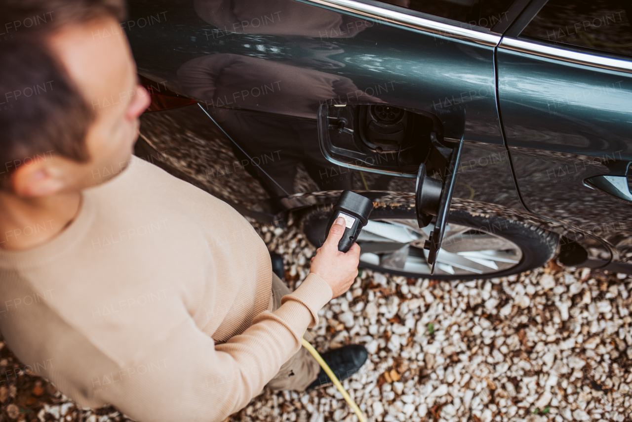 Close up of man charging electric car, plugging charger in charging port.