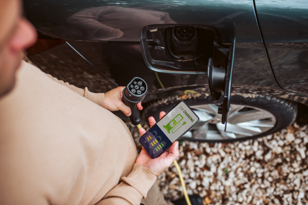 High angle view of man charging electric car, checking charging app, close up.