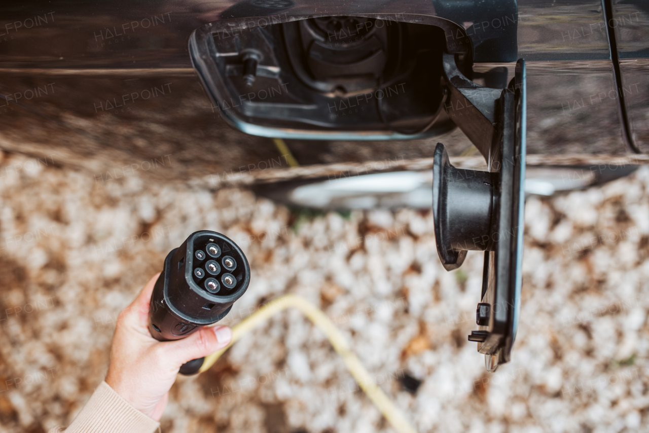 Man charging electric car, hodding charger in his hand.