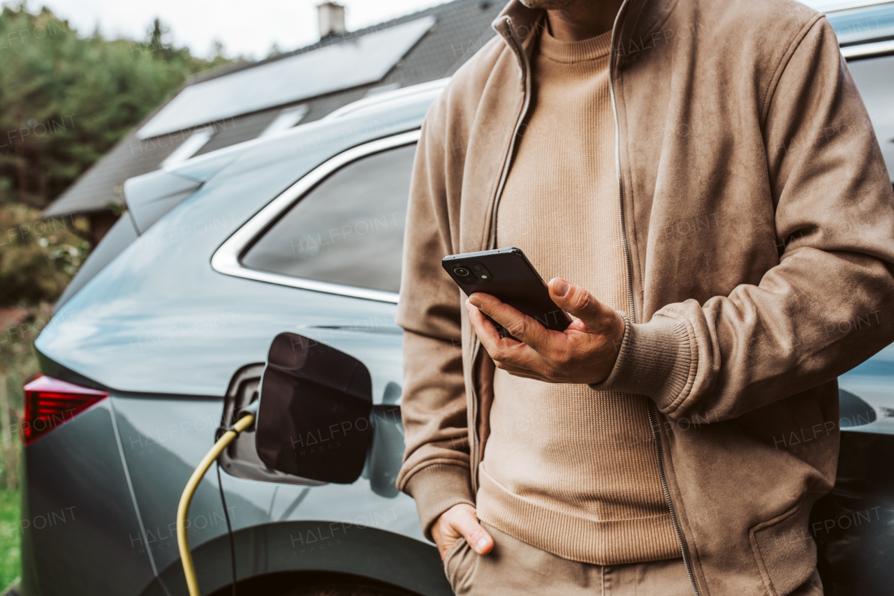 Man charging electric car, checking progress in app. Vehicle with charger in charging port.