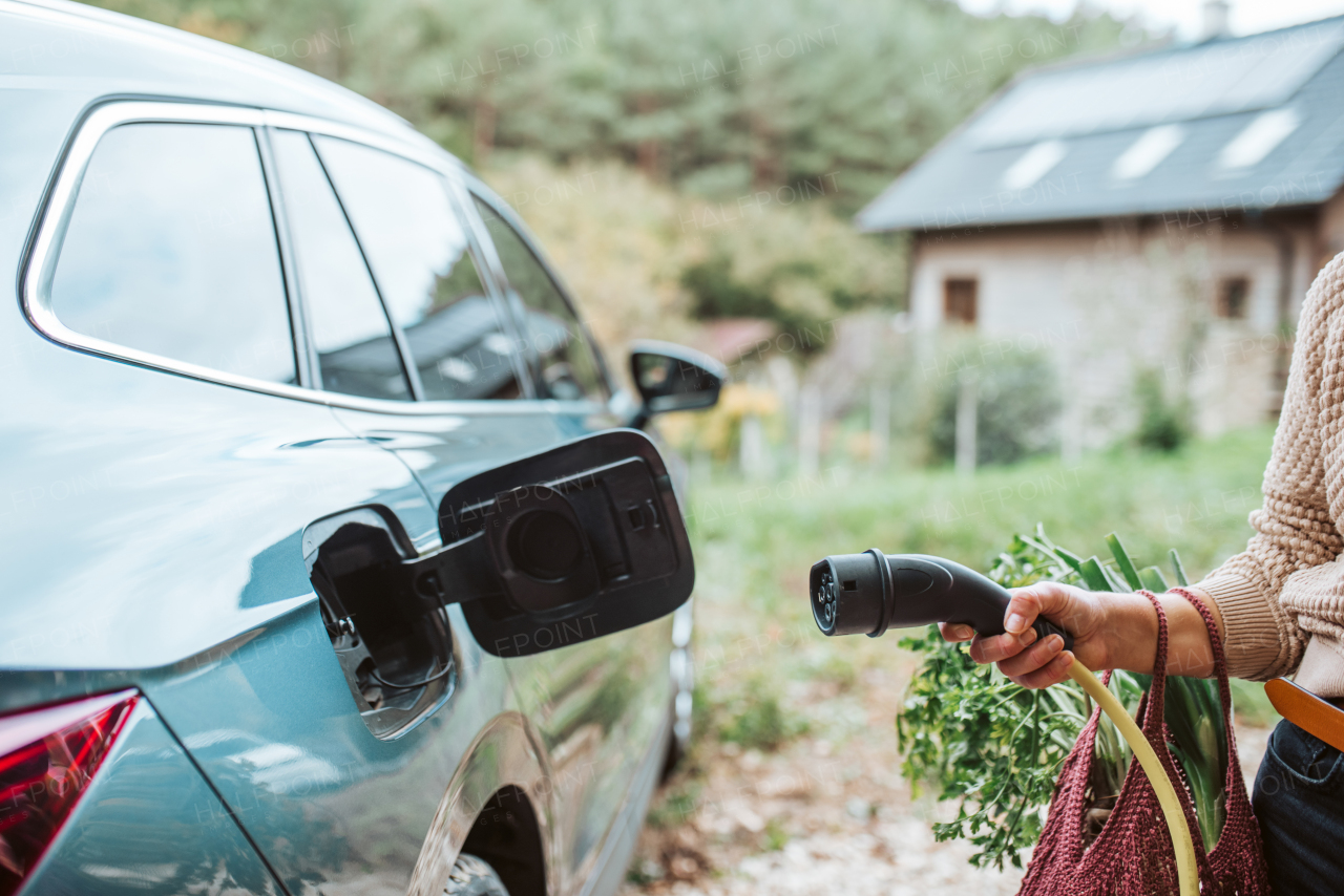 Woman charging electric car, plugging charger in charging port, close up.