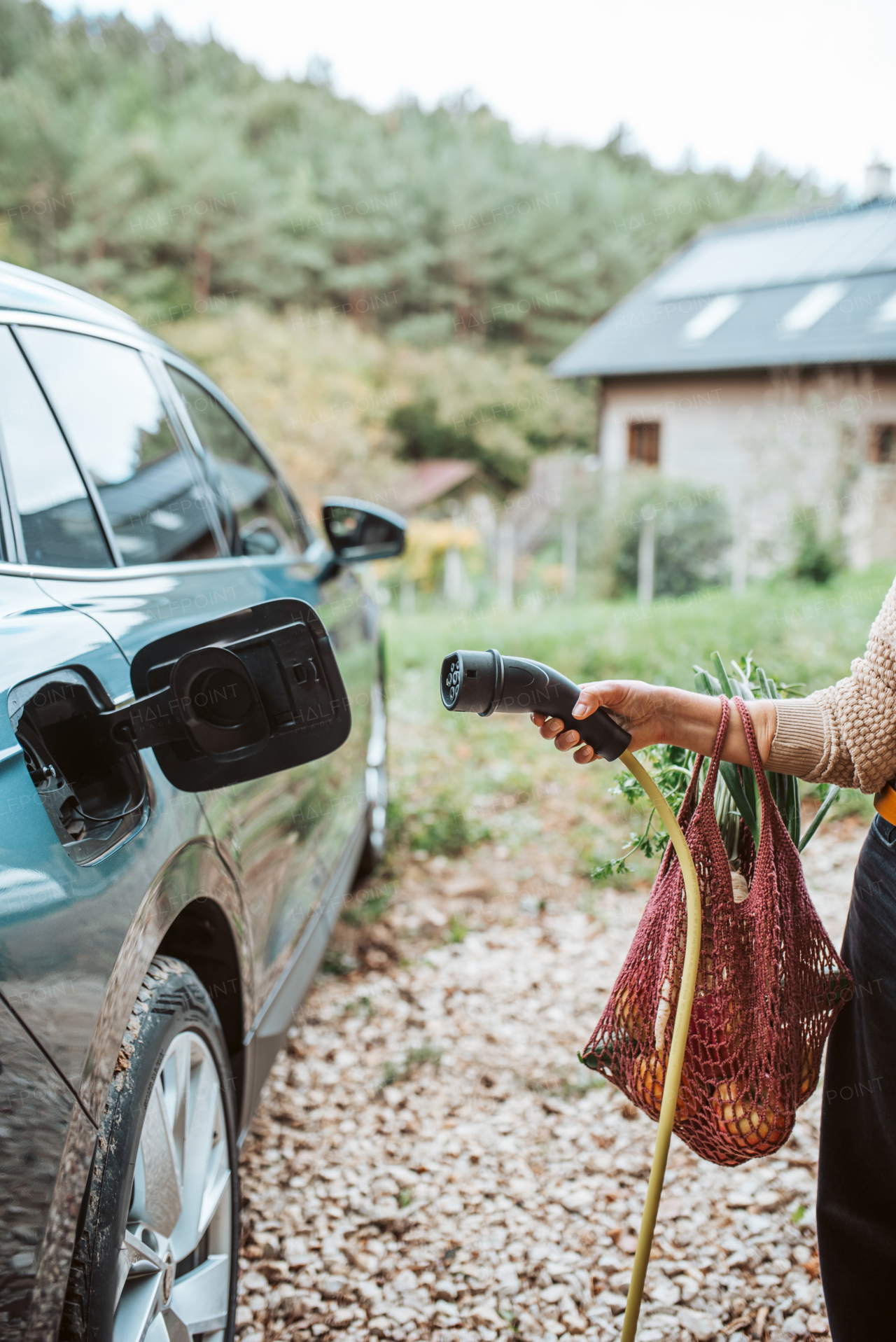 Woman charging electric car, plugging charger in charging port, close up.