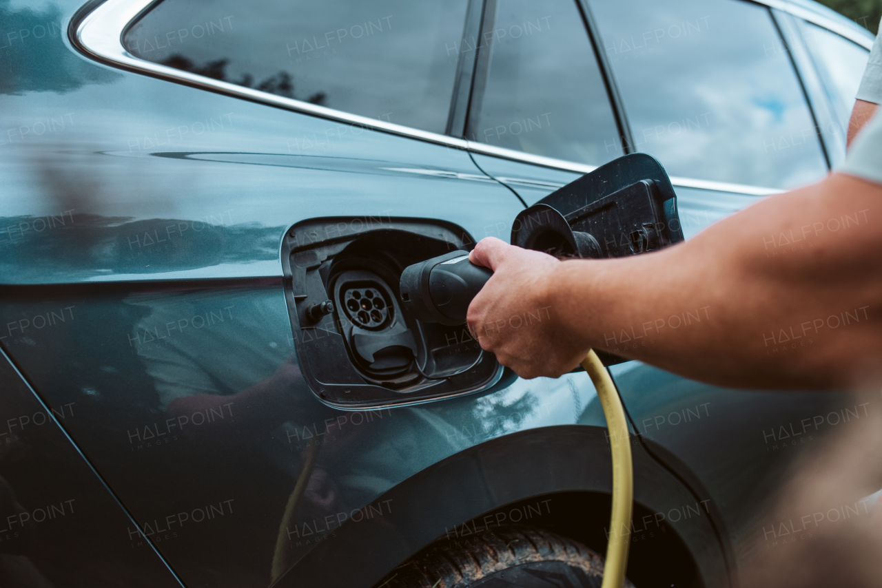 Close up of man charging electric car, plugging charger in charging port.