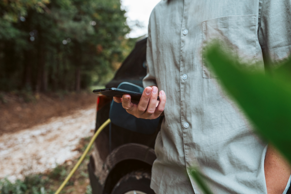 Man charging electric car, checking progress in app, close up.