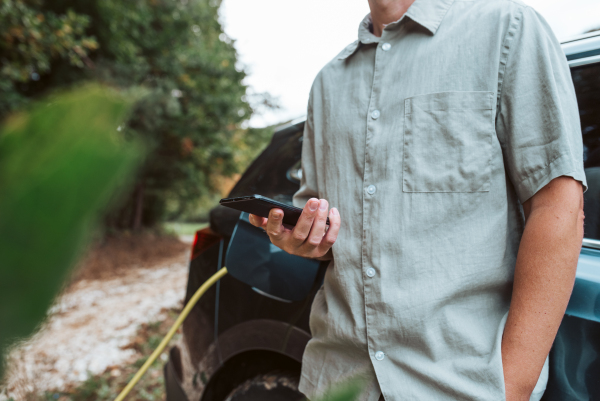 Man charging electric car, checking progress in app, close up.