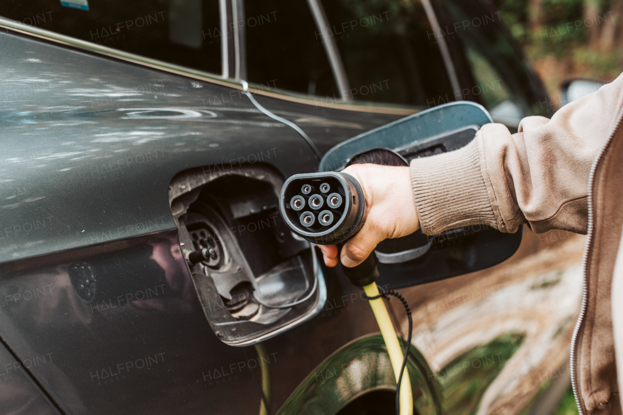 Man charging electric car, hodding charger in his hand.