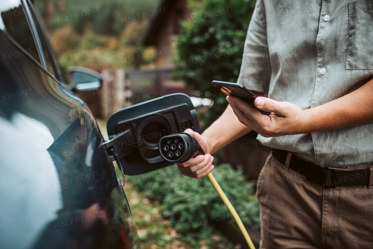 Man charging electric car, checking progress in app, close up.