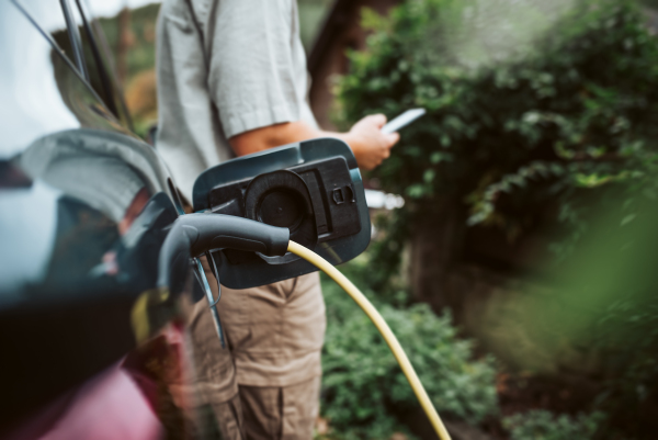 Man charging electric car, checking progress in app, close up.