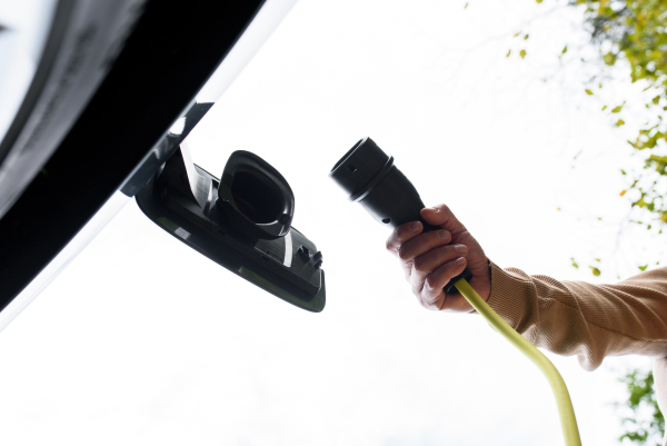 Low angle view of man charging electric car, plugging charger in charging port.