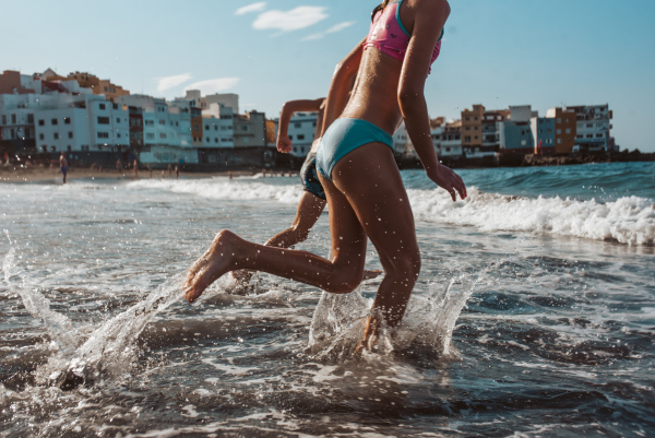 Siblings running across the beach into sea. Concept of family beach summer vacation with kids.