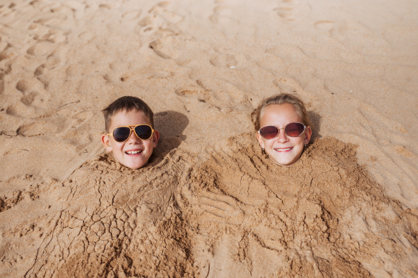 Children buried in sand on the beach, having fun during a family vacation.