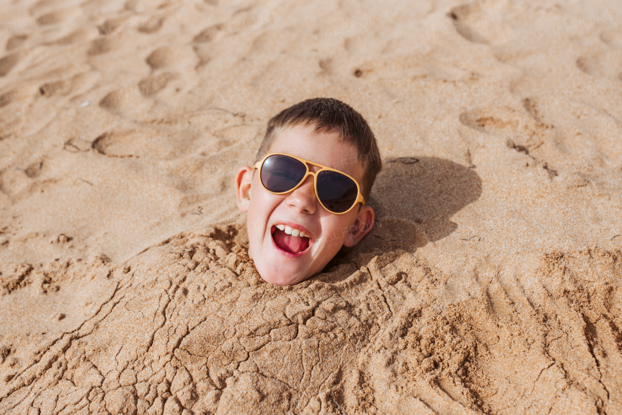 Boy buried in sand on the beach, having fun during a family vacation.