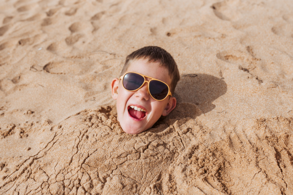 Boy buried in sand on the beach, having fun during a family vacation.